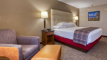 Una habitación de hotel con una cama, una silla, una mesita de noche y una lámpara.