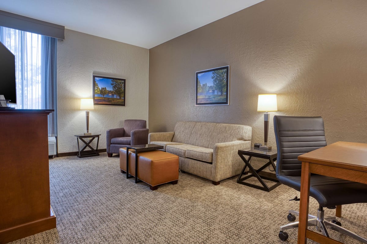 A hotel room with a sofa, armchair, ottoman, desk, and two lamps.