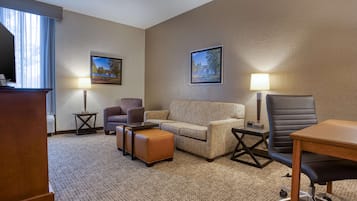 A hotel room with a sofa, armchair, ottoman, desk, and two lamps.