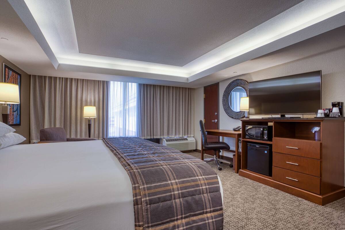 A hotel room with a large bed, a desk with a flat-screen TV, a microwave, and a minibar.