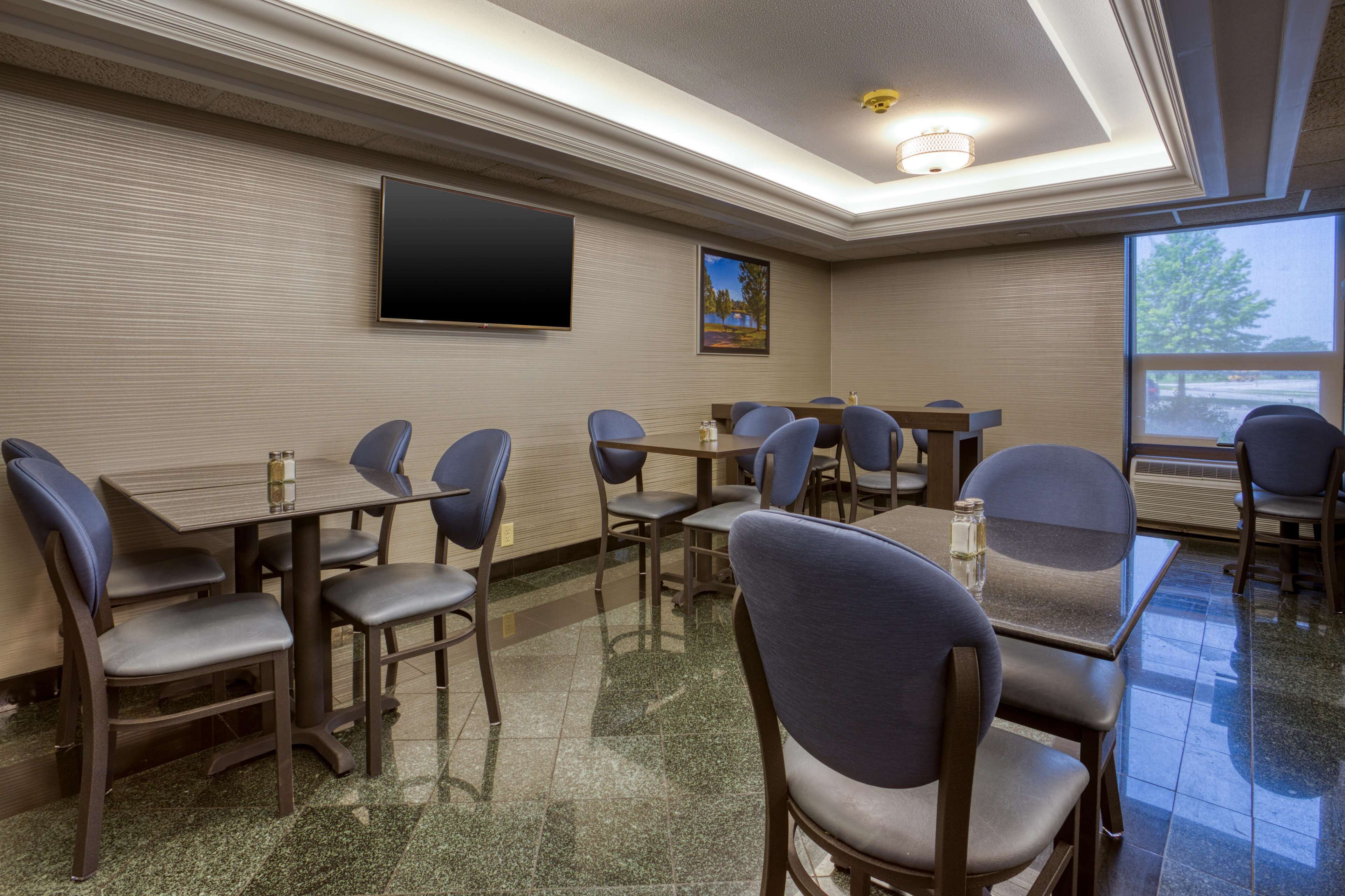 A conference room with multiple tables and chairs, a flat-screen TV, and a large window with a view.