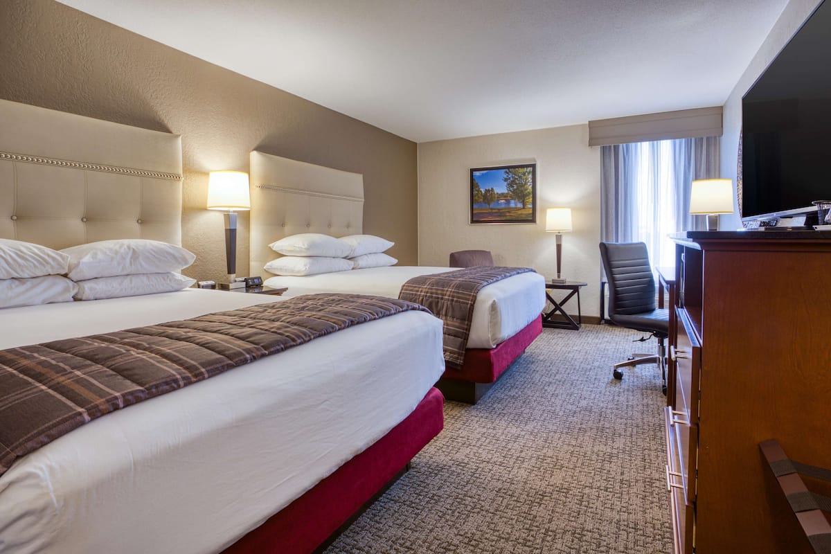 A hotel room with two beds, a desk, a chair, a television, and a painting on the wall.