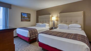 A hotel room with two beds, a desk, and a lamp.