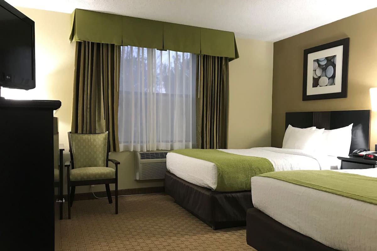 A hotel room with two beds, a chair, a desk, and a window with curtains.