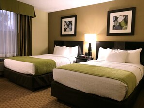 A hotel room with two beds, a nightstand with a lamp, and framed artwork on the walls. - Navajoland Hotel of Tuba City (Tuba City)