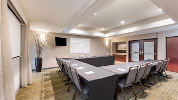 A conference room with a long table, chairs, a projector screen, and a large vase with branches.