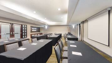 A conference room with long tables, chairs, a projector screen, and a whiteboard.