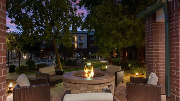An outdoor patio with a circular stone fire pit surrounded by wicker furniture and cushions. - Sonesta Select Tempe Downtown (Tempe)