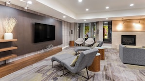 A modern living room with a flat-screen TV, grey sofas, a fireplace, and a large window. - Sonesta Select Tempe Downtown (Tempe)