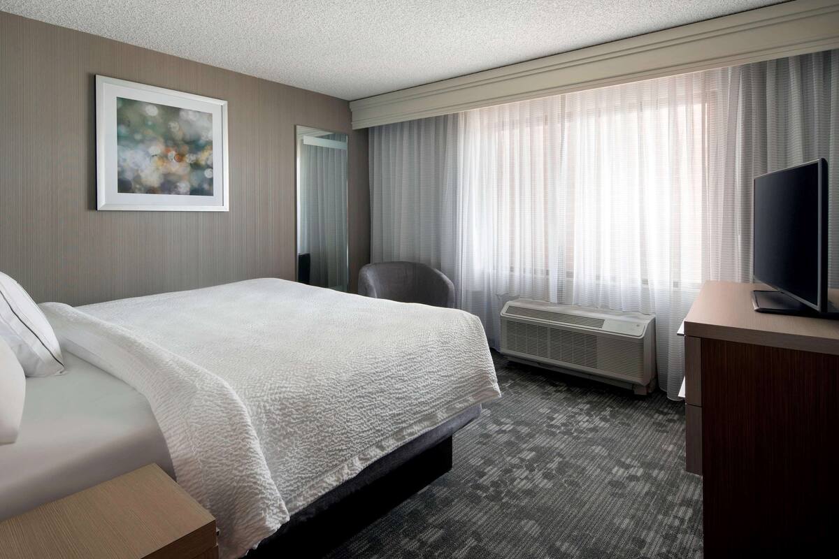 A hotel room with a large bed, a desk with a television, a chair, and a window with curtains.