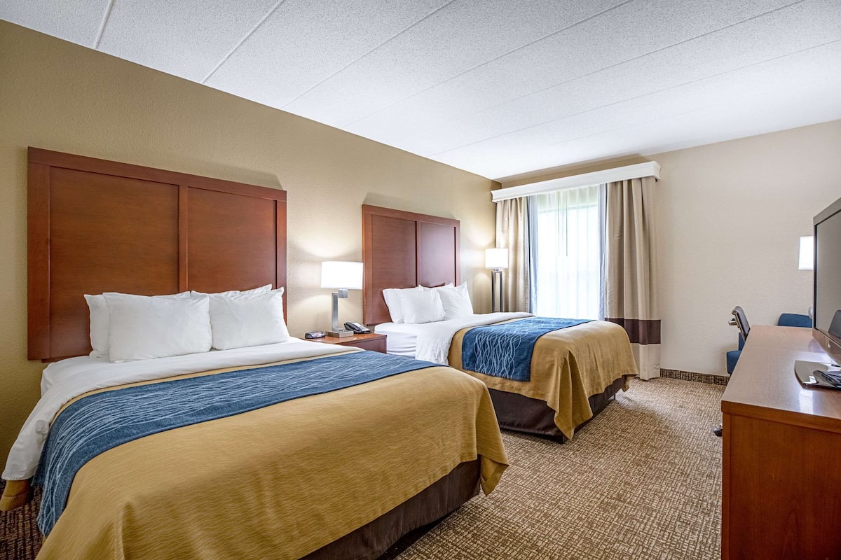 A hotel room with two beds, a desk, and a TV.