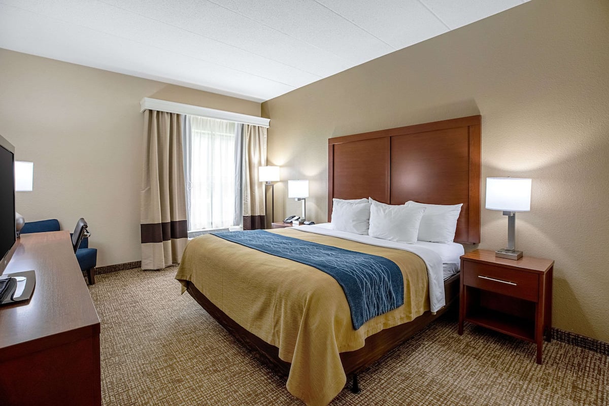 A hotel room with a large bed, bedside tables, a desk, and a television.