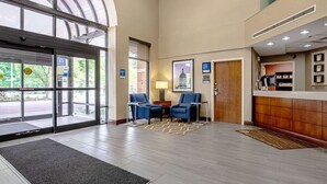 A lobby with a reception desk, two blue chairs, a large window, and a door with a glass entrance. - Comfort Inn Indianapolis North - Carmel (Indianapolis)