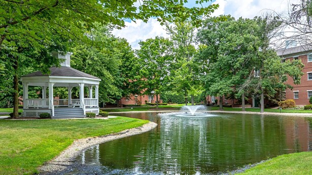 A gazebo with a pond and fountain, surrounded by lush greenery and brick buildings. - Comfort Inn Indianapolis North - Carmel (Indianapolis)