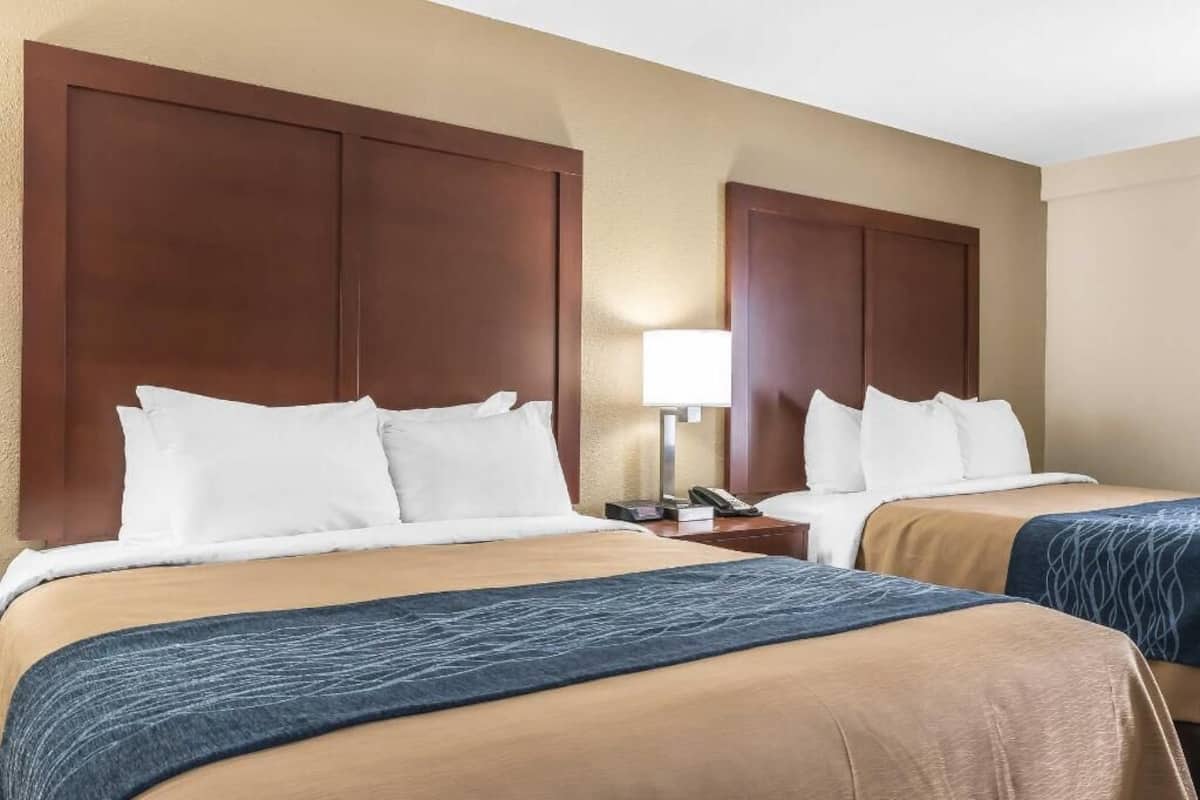 A hotel room with two beds, each with a wooden headboard, a bedside table with a lamp, and a telephone.