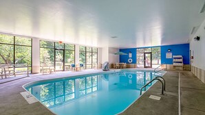 An indoor swimming pool with clear glass walls, a blue wall, and a sunlit room with windows and chairs. - Comfort Inn Indianapolis North - Carmel (Indianapolis)