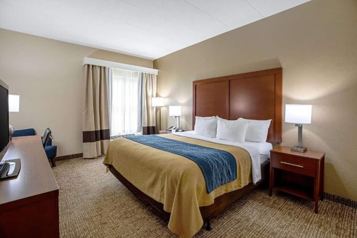 A hotel room with a bed, bedside tables, a desk, and a television.
