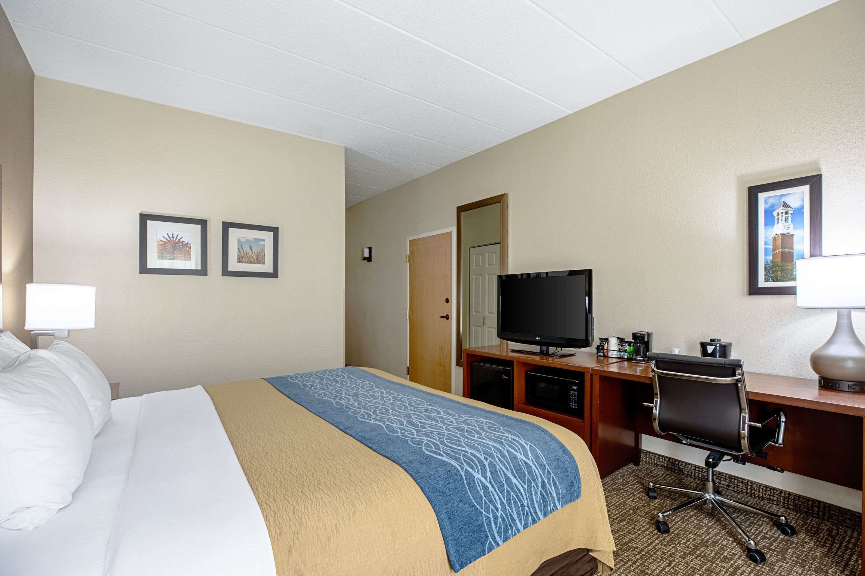 Una habitación de hotel con cama, escritorio, televisión y una silla.