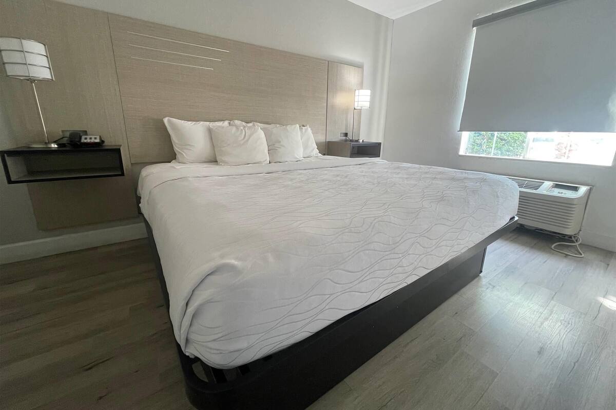 Una habitación de hotel moderna con una cama grande, mesitas de noche, una lámpara y una ventana con vistas.