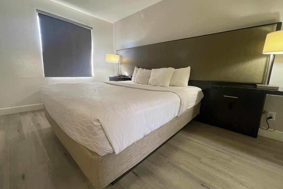 Una habitación de hotel moderna con una cama grande, dos mesitas de noche, un cabecero y un ventanal.