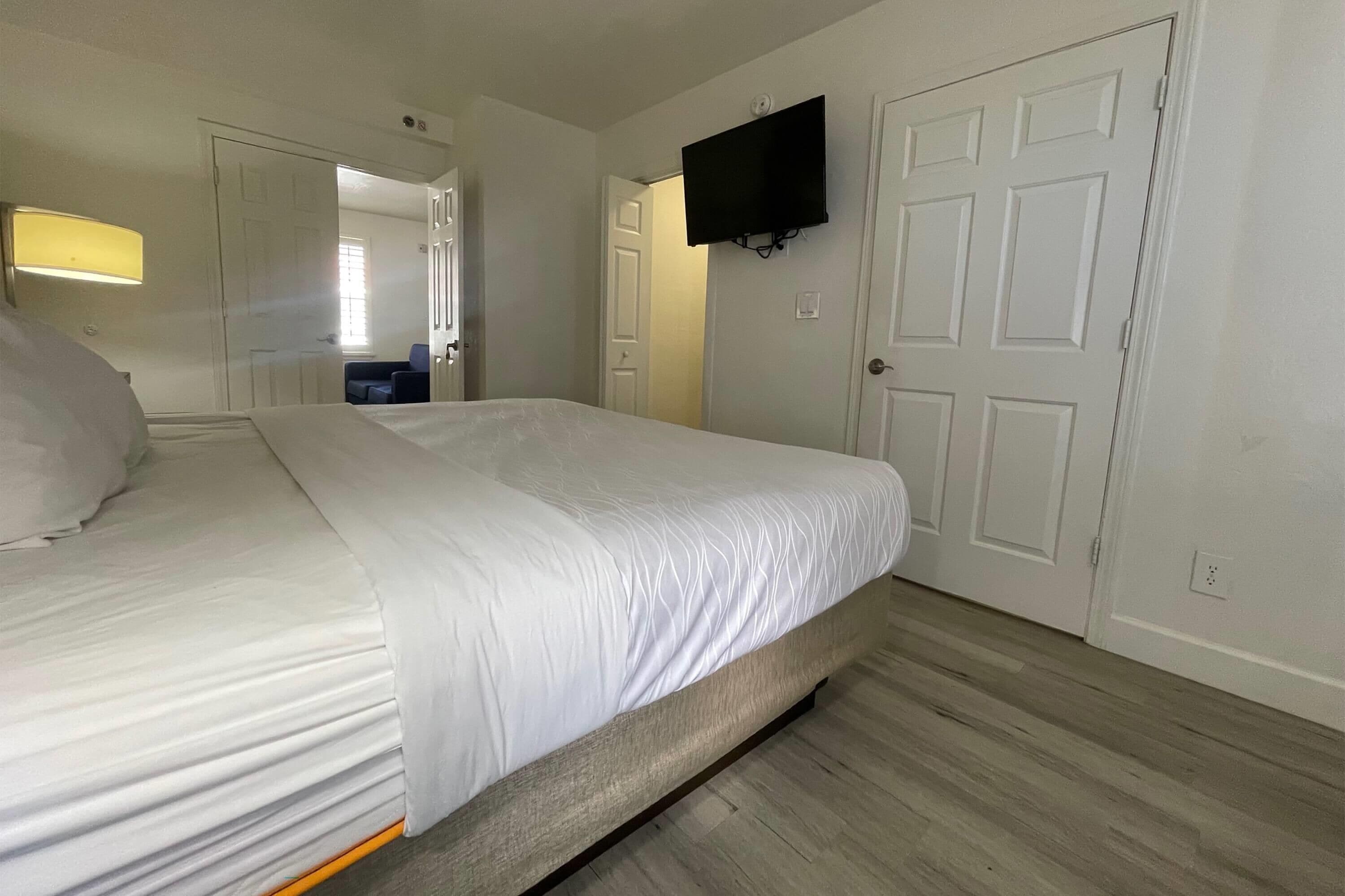 Une chambre d’hôtel avec un lit, un téléviseur fixé au mur et une porte donnant sur une autre pièce.