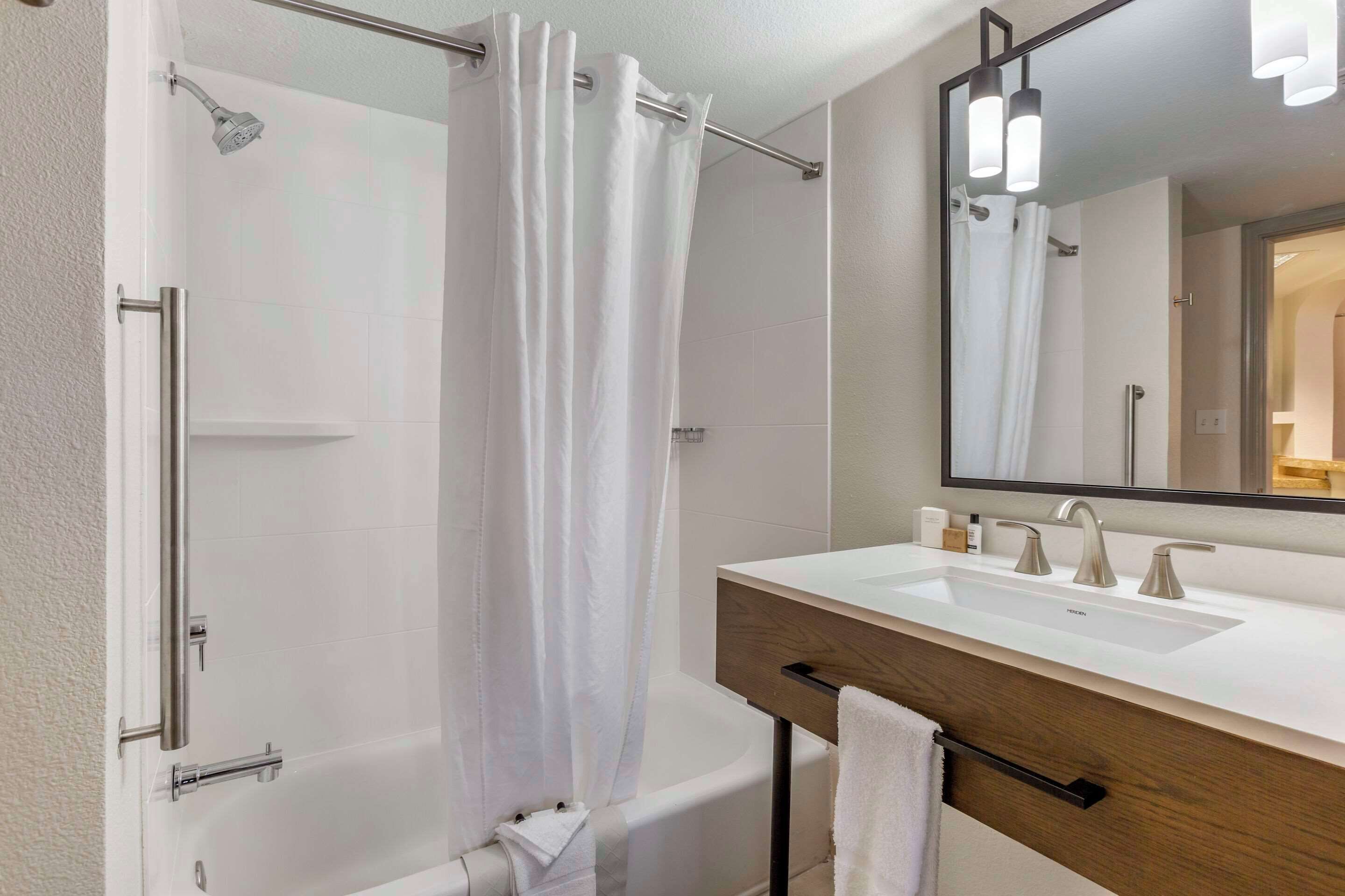 A modern bathroom with a shower, a bathtub, a vanity with a mirror, and a towel rack.