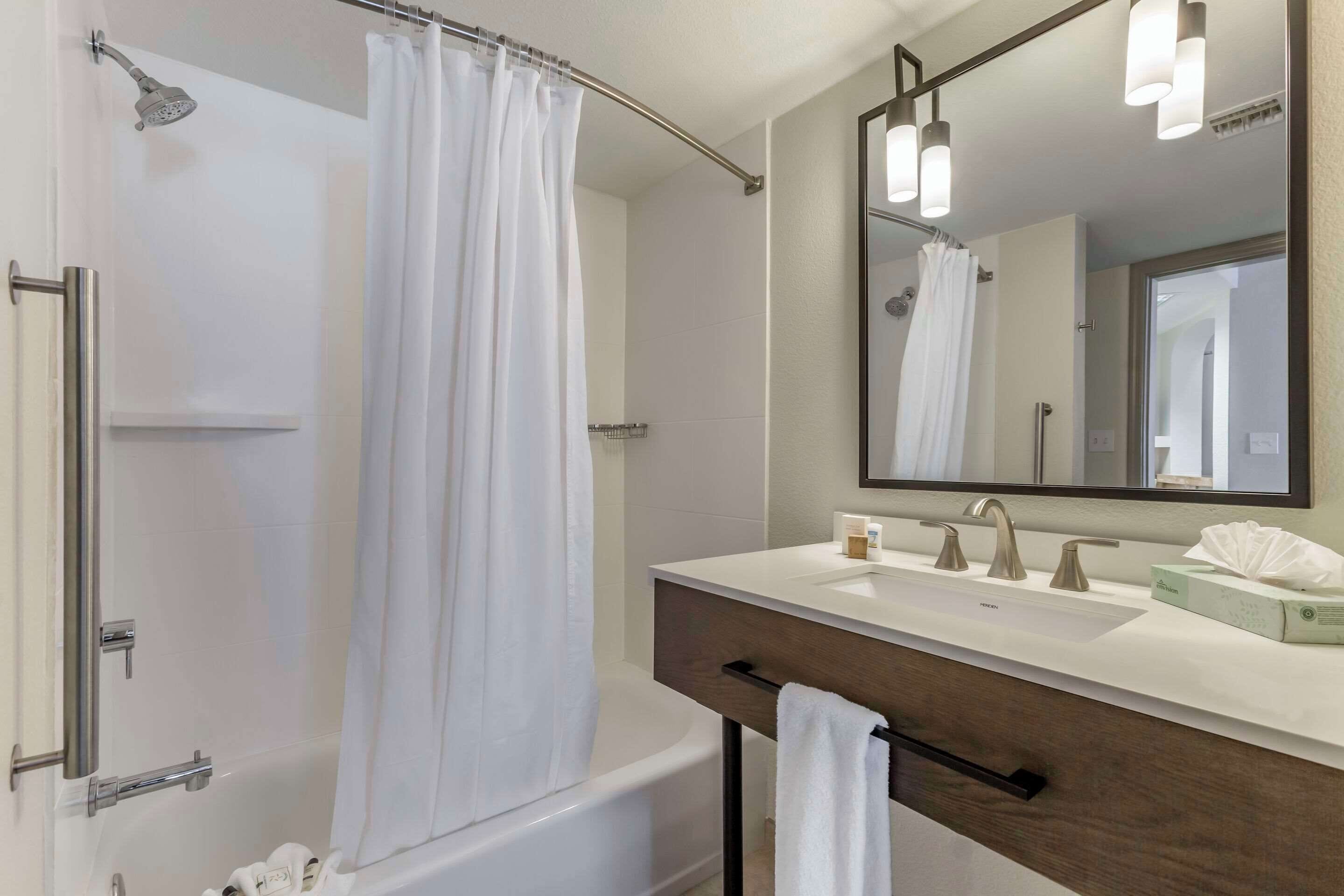 Un baño moderno con bañera, ducha, tocador con lavamanos y espejo.