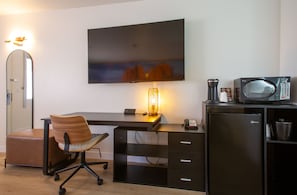 A modern office space with a desk, chair, flat-screen TV, lamp, microwave, and refrigerator.