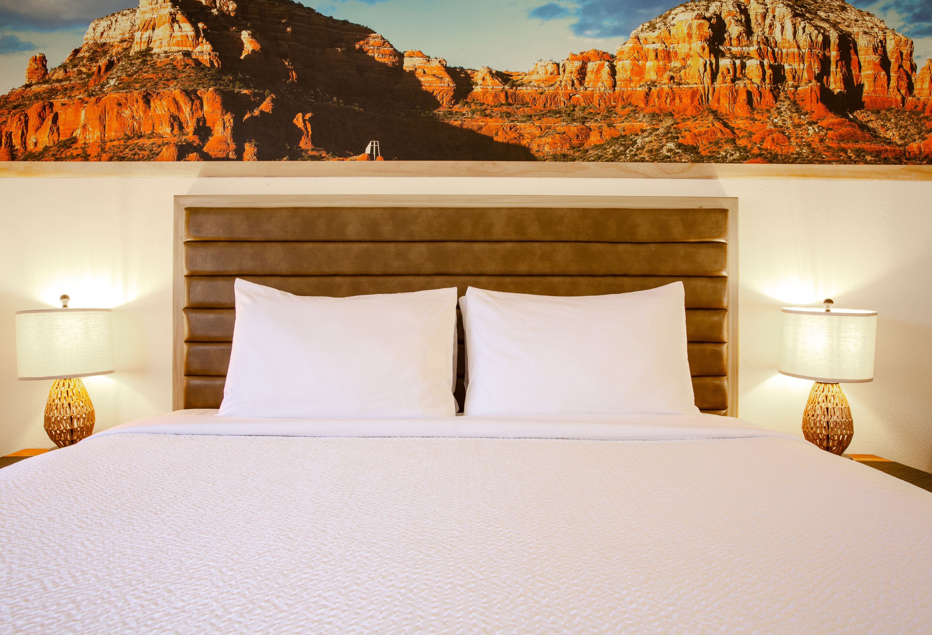 Una habitación de hotel con una cama grande, dos lámparas de noche y un mural con vistas a la montaña.