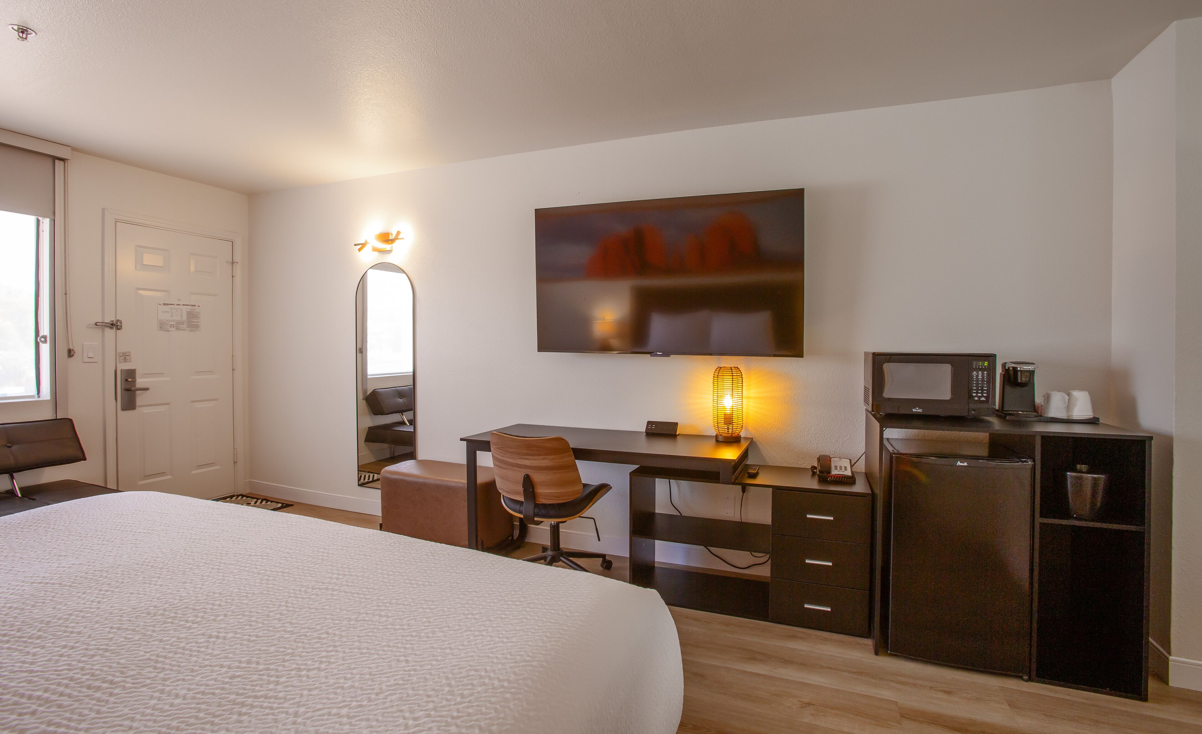 A hotel room with a bed, desk, chair, TV, microwave, and coffee maker.