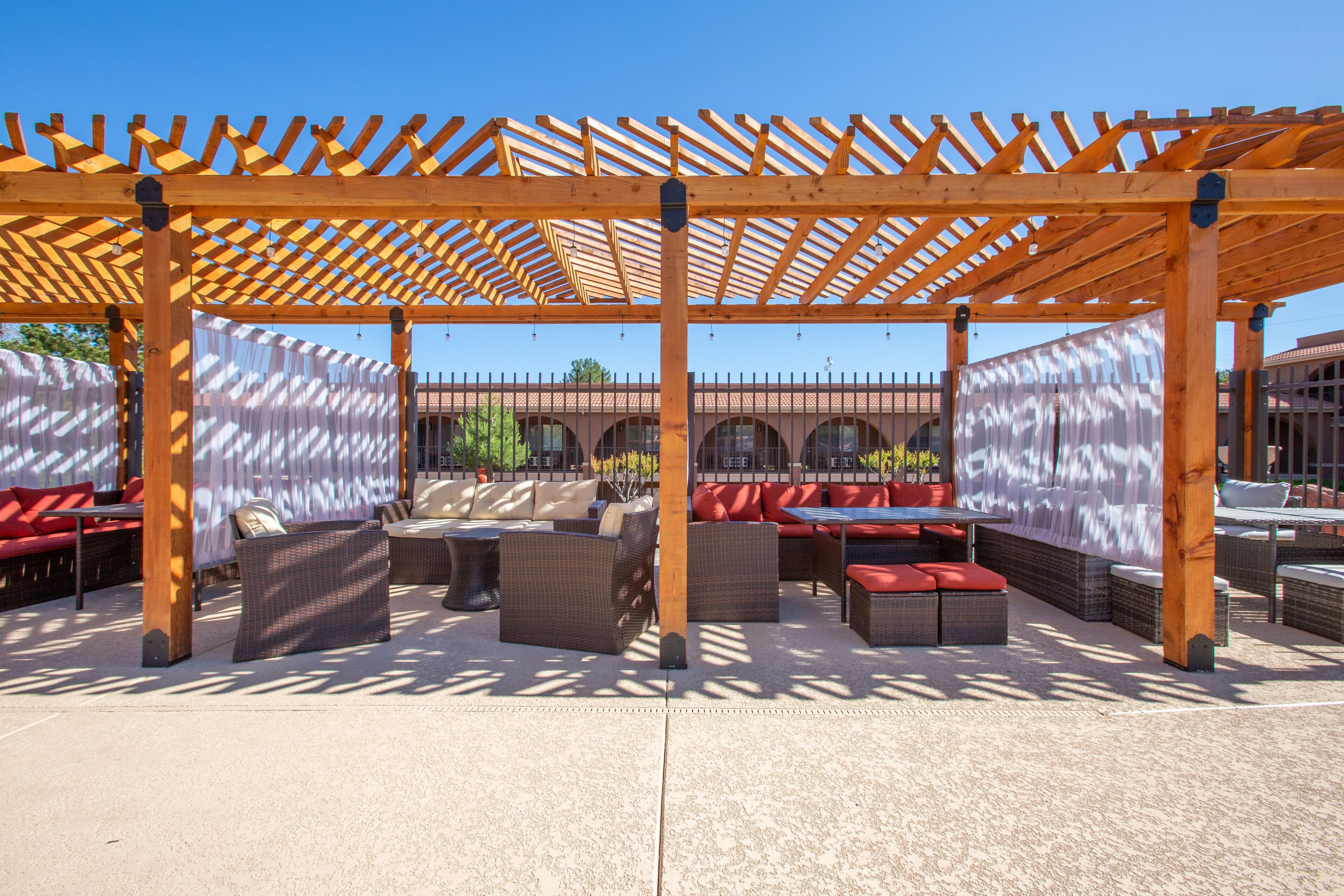 An outdoor patio area with wooden pergola, wicker furniture, and red cushioned seating.