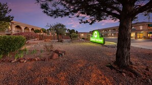 A hotel entrance with a sign reading "GreenTree Inn," surrounded by a gravel area with a large tree and a building with arched windows in the background.