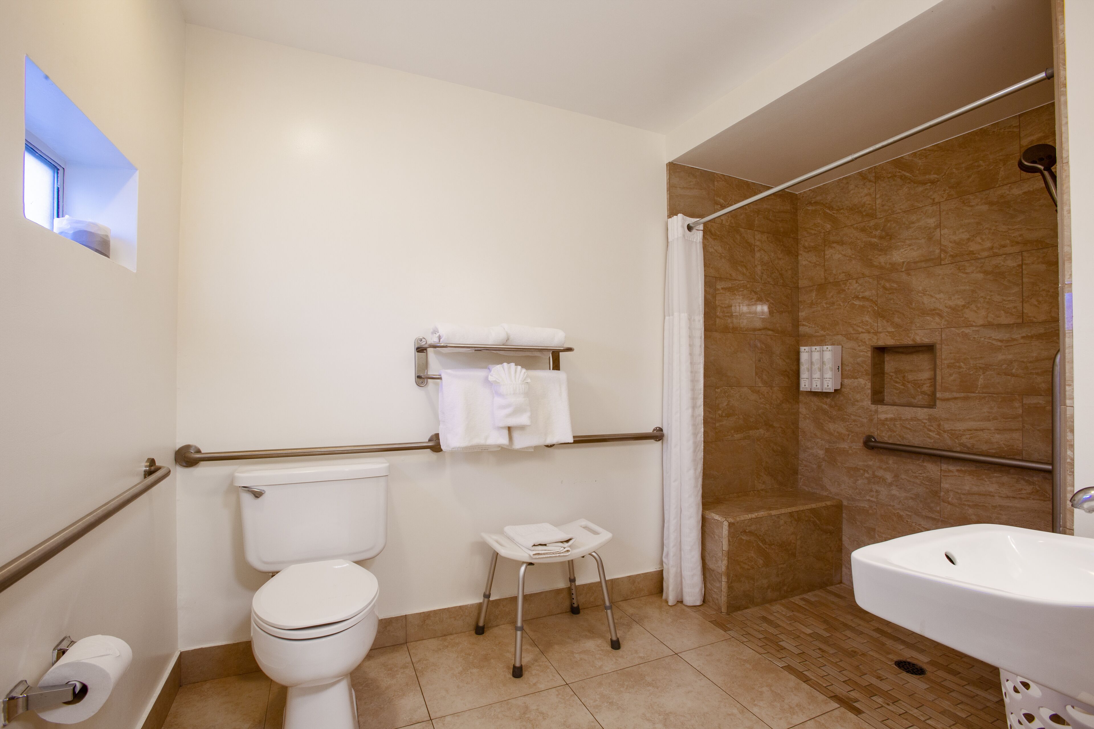 A bathroom with a toilet, a sink, a shower with a glass door, and a small step stool.