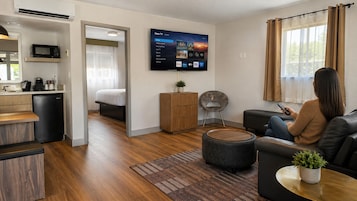 Una sala de estar moderna con un televisor de pantalla plana montado en la pared, un sofá, una mesa de centro y un comedor con microondas.