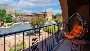A balcony with a hanging chair, a view of a parking area, and a building with a desert landscape in the background.