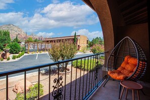 A balcony with a hanging chair, a view of a parking area, and a building with a desert landscape in the background.