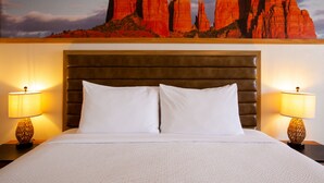 A hotel room with a large bed, two bedside lamps, and a wall mural of red rock formations.