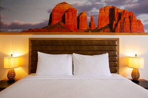 A hotel room with a large bed, two bedside lamps, and a wall mural of red rock formations.