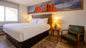 A hotel room with a large bed, a green armchair, a painting of rock formations, and two bedside lamps. - GreenTree Inn Sedona (Sedona)