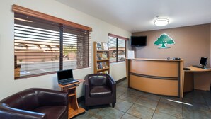 A reception area with a desk, two leather chairs, a bookshelf, and a wall-mounted TV. - GreenTree Inn Sedona (Sedona)