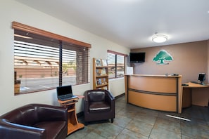 A reception area with a desk, two leather chairs, a bookshelf, and a wall-mounted TV.