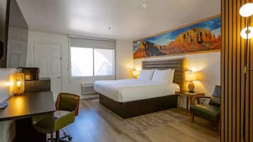 Une chambre d’hôtel équipée d’un lit, d’un bureau, d’une chaise et d’un tableau représentant un paysage de montagne.
