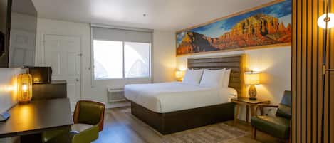 Een hotelkamer met een bed, bureau, stoel en een schilderij van een berglandschap.