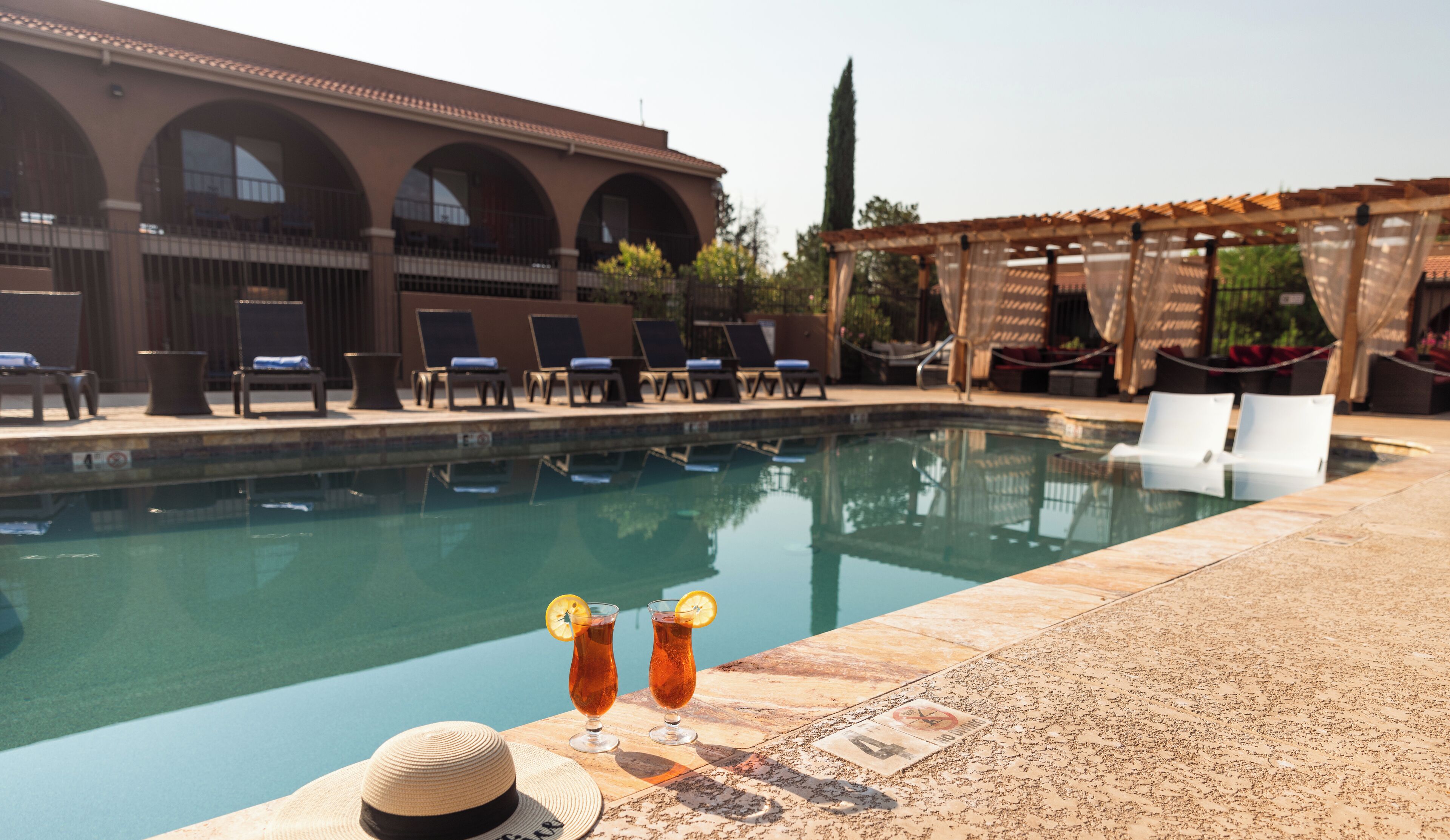 A pool area with lounge chairs and a building with arched windows in the background.