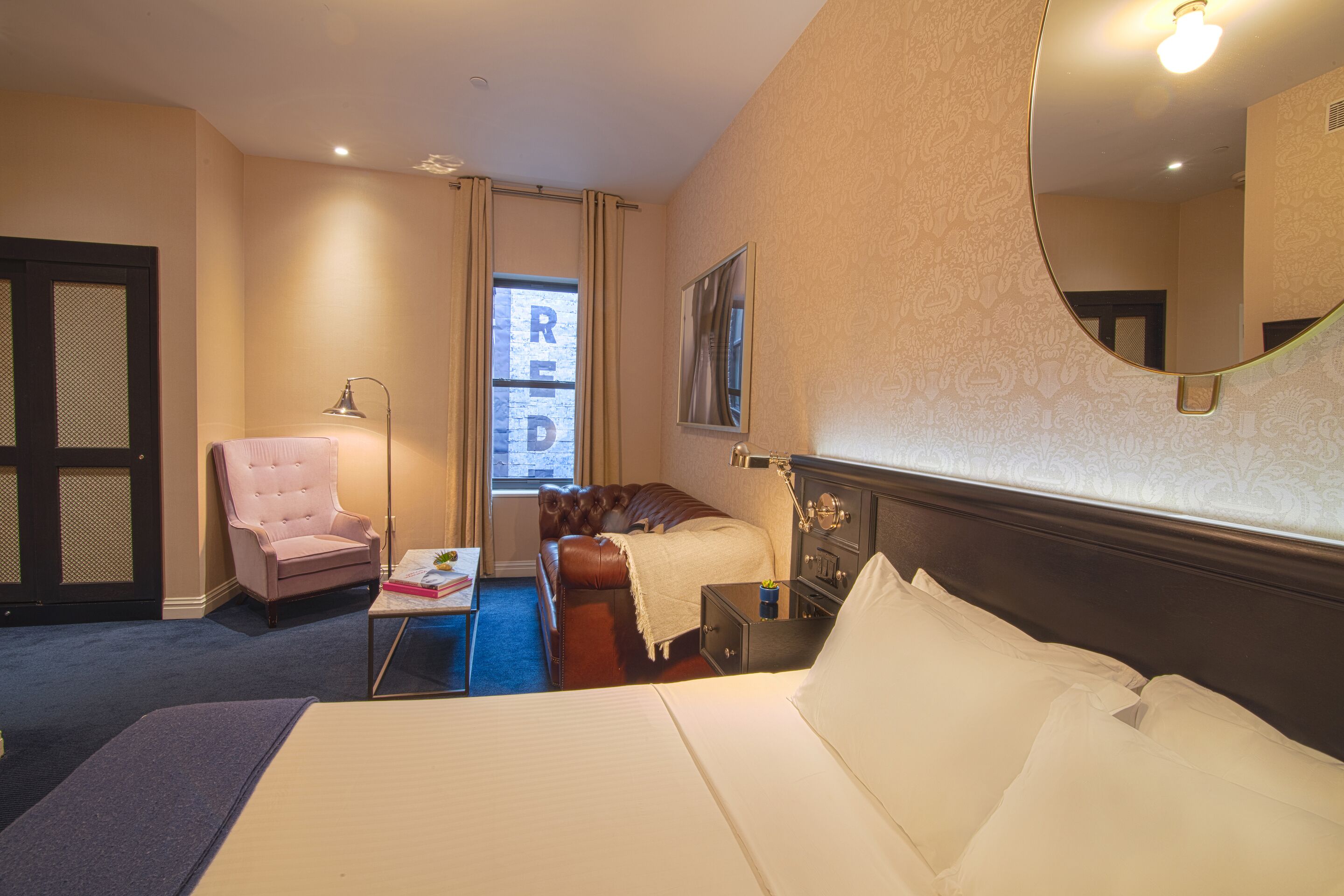 A hotel room with a large bed, a chair, a desk, a dresser, and a window with curtains.