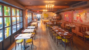 A restaurant with long tables, yellow chairs, and a brick wall with graffiti. - The Frederick Hotel Tribeca, a Small Luxury Hotel (New York)