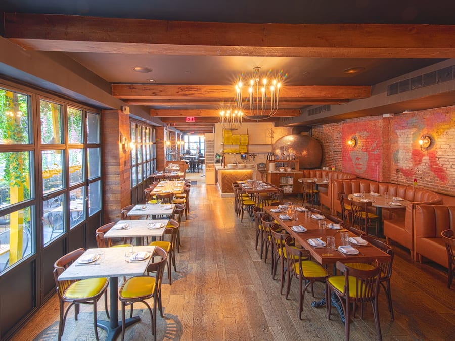 Un restaurante con mesas largas, sillas amarillas y una pared de ladrillo con grafitis.
