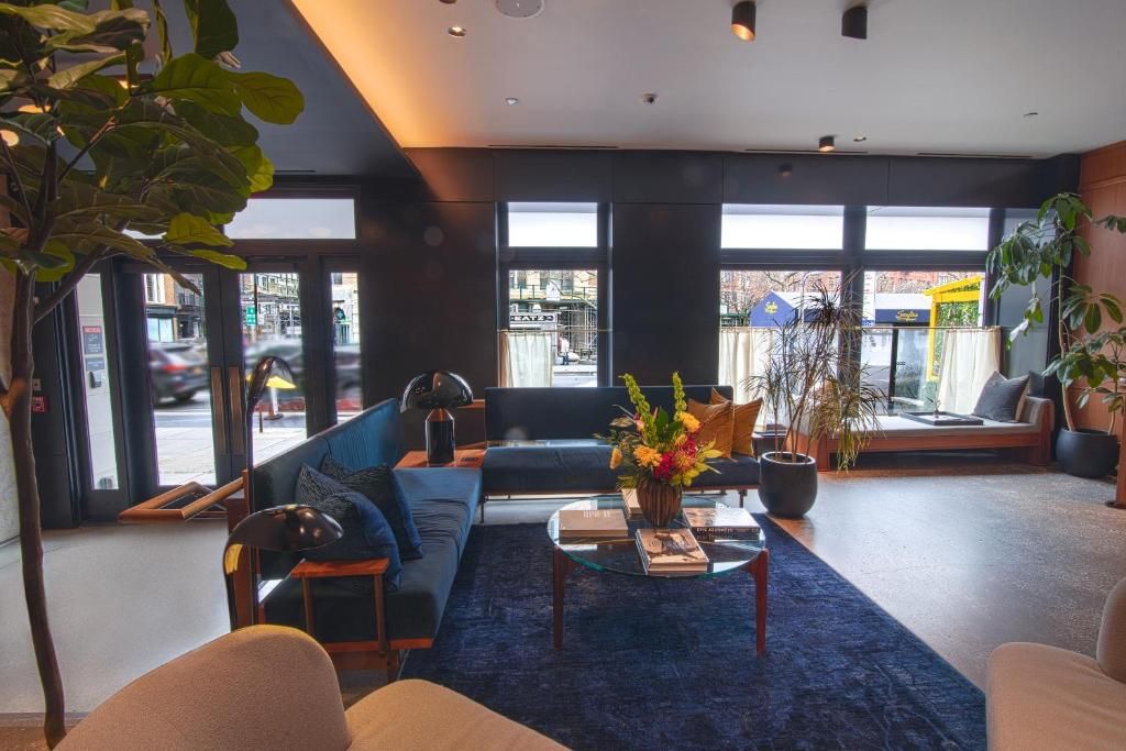 A modern hotel lobby with a blue sofa, a coffee table with books, and a large window offering a view of the street.
