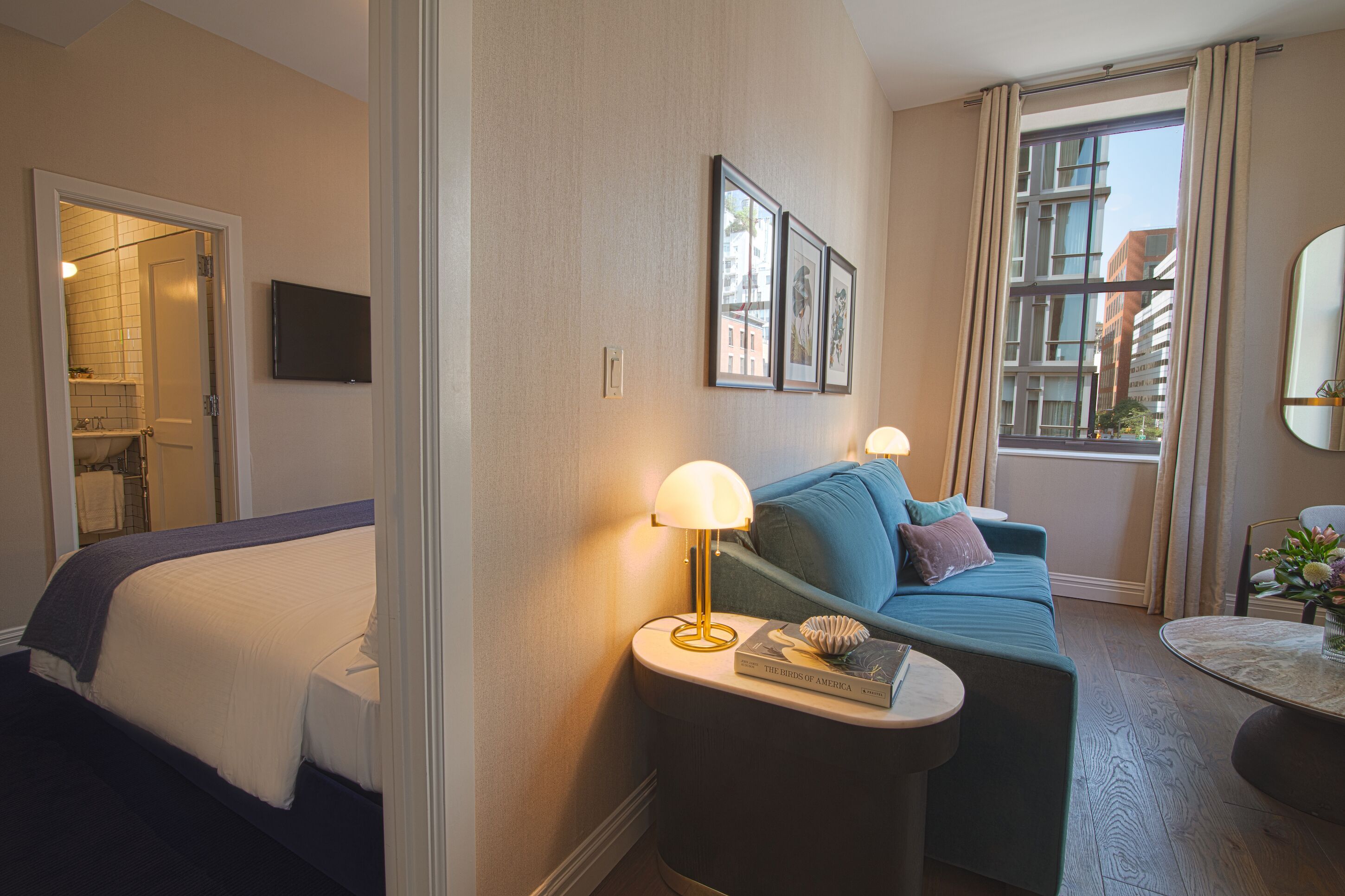 Een hotelkamer met een bed, een bank, een lamp, een tafeltje en een raam met gordijnen.