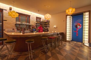 Een bar met een barman, barkrukken en een goed gevulde plank met flessen.